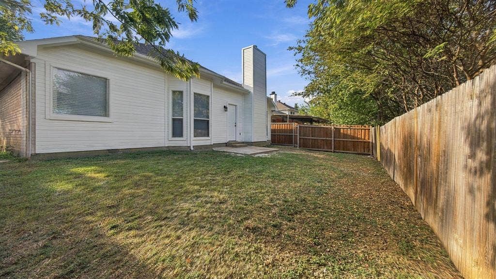 Backyard featuring white horizontal siding, a prominent exterior chimney, a stone patio, and a wood privacy fence