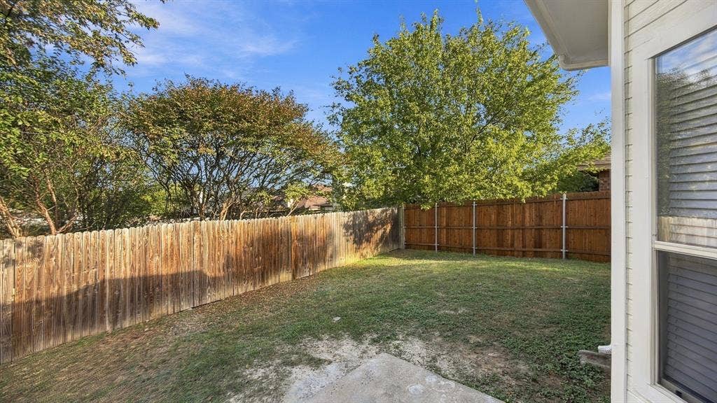 Private backyard featuring a wood privacy fence, concrete patio, grass lawn, and mature trees
