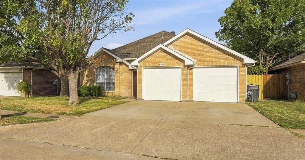 Single-story exterior featuring light brick masonry, a gabled roofline, a two-car garage, and a concrete driveway