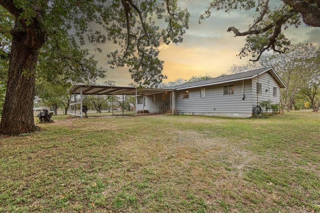 3907 Rogers Hill Road, Waco, TX 76705 Single-story exterior featuring light-toned horizontal siding, a gabled roofline, an attached metal carport, and expansive grounds shaded by mature trees