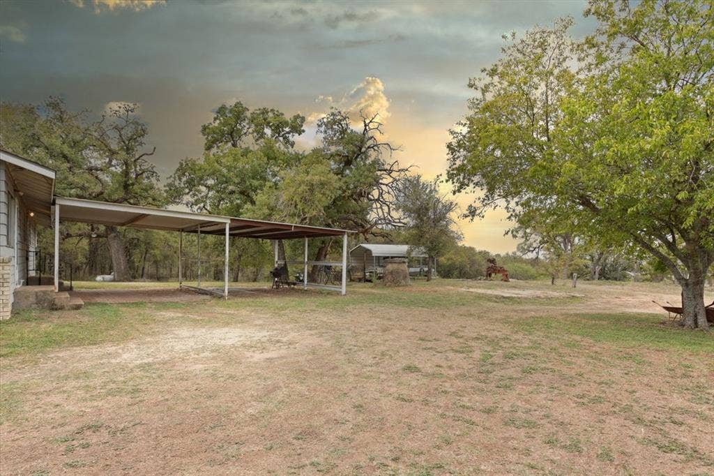 3907 Rogers Hill Road, Waco, TX 76705 Expansive acreage featuring mature trees, a metal-roofed carport, and a secondary metal storage structure
