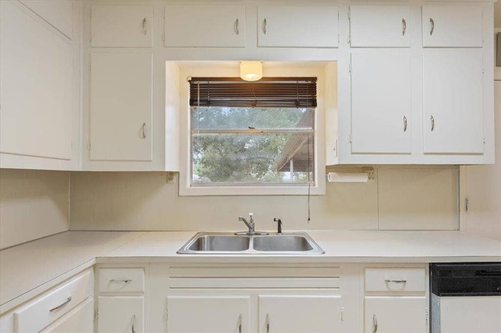 3907 Rogers Hill Road, Waco, TX 76705 Kitchen featuring white cabinetry, solid-surface countertops, dual-basin stainless steel sink with pull-out sprayer faucet, and natural light via a central window