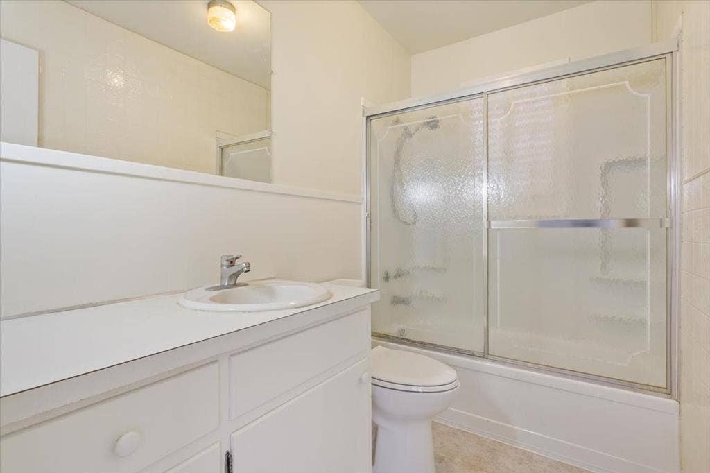 3907 Rogers Hill Road, Waco, TX 76705 Bathroom featuring a white vanity cabinet with a solid surface countertop, integrated vanity sink, polished chrome faucet, and a shower-tub combination enclosed by sliding textured glass doors