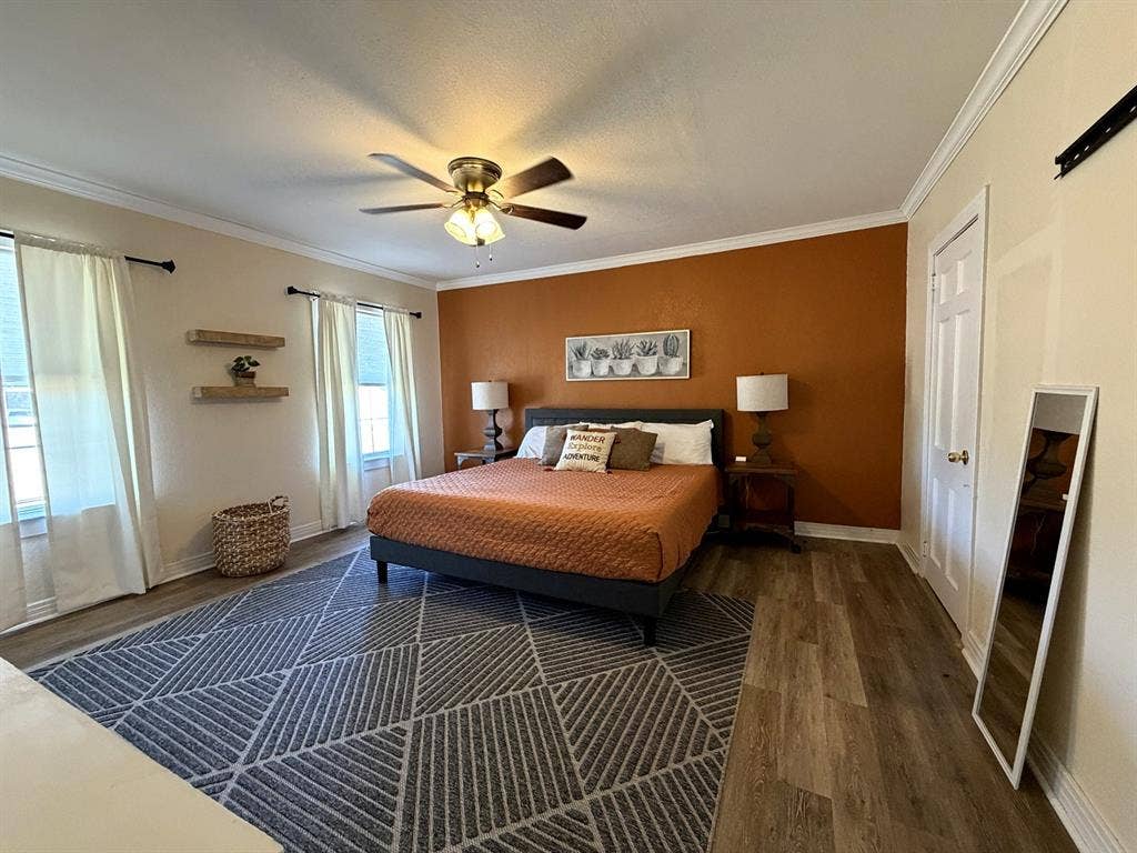 201 S Jones Street, Granbury, TX 76048 Room featuring wood-finish flooring, accent wall, ceiling fan with integrated lighting, crown molding, and wall-mounted shelving