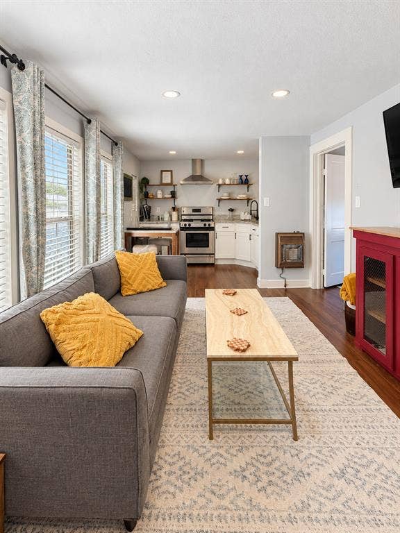 201 S Jones Street, Granbury, TX 76048 Open-concept floor plan featuring wood-finish flooring, stainless steel range with overhead chimney hood, white cabinetry, and recessed lighting