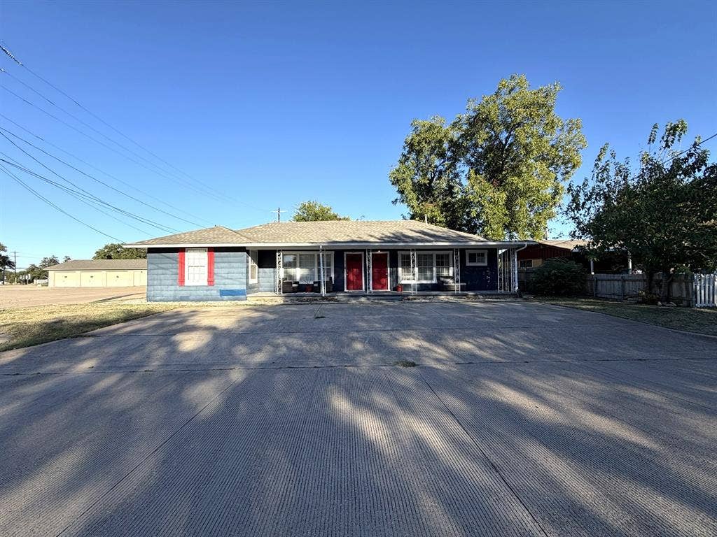 201 S Jones Street, Granbury, TX 76048 Single-story exterior featuring blue siding, red accent shutters, two separate entry doors, a wide concrete driveway, and a covered front porch