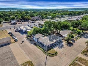 201 S Jones Street, Granbury, TX 76048 Aerial perspective of a single-story structure with a multi-gabled roof, featuring an attached garage, extensive paved parking area, and mature landscaping