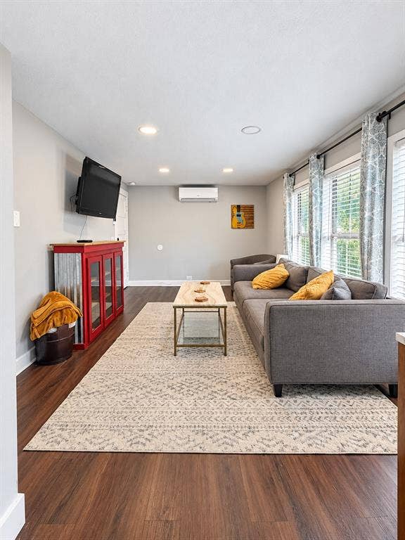 201 S Jones Street, Granbury, TX 76048 Living area featuring wood-finish flooring, recessed lighting, and a wall-mounted ductless climate control unit, characterized by large windows with horizontal blinds