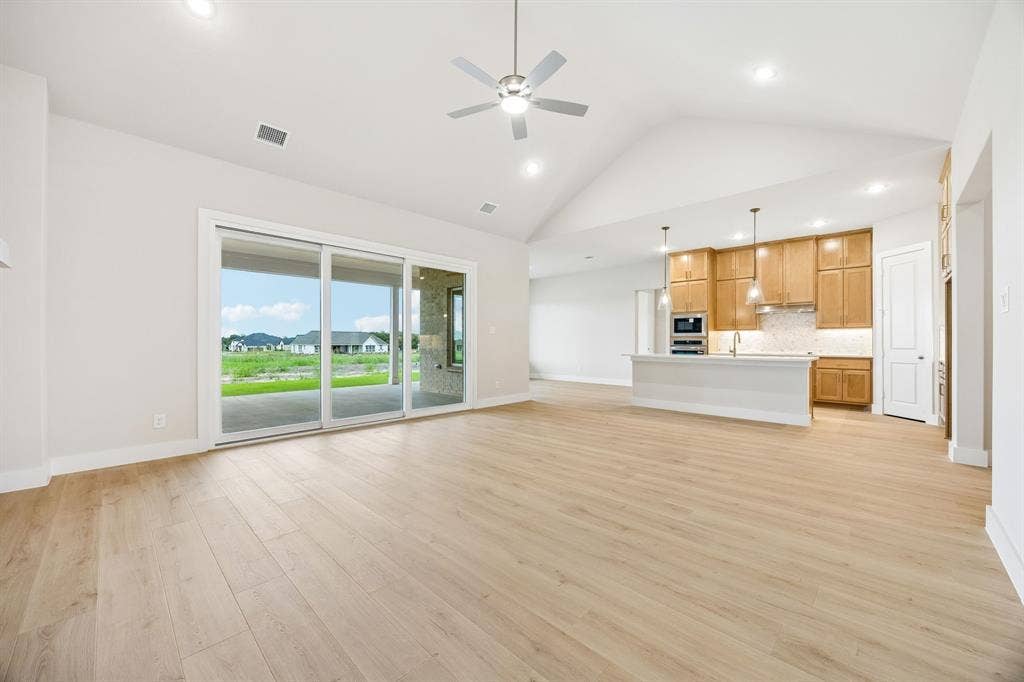 108 Swan Lake Drive, Waxahachie, TX 75165 Open-concept interior featuring vaulted ceilings, wood-finish flooring, sliding glass doors, a kitchen island, and built-in cabinetry