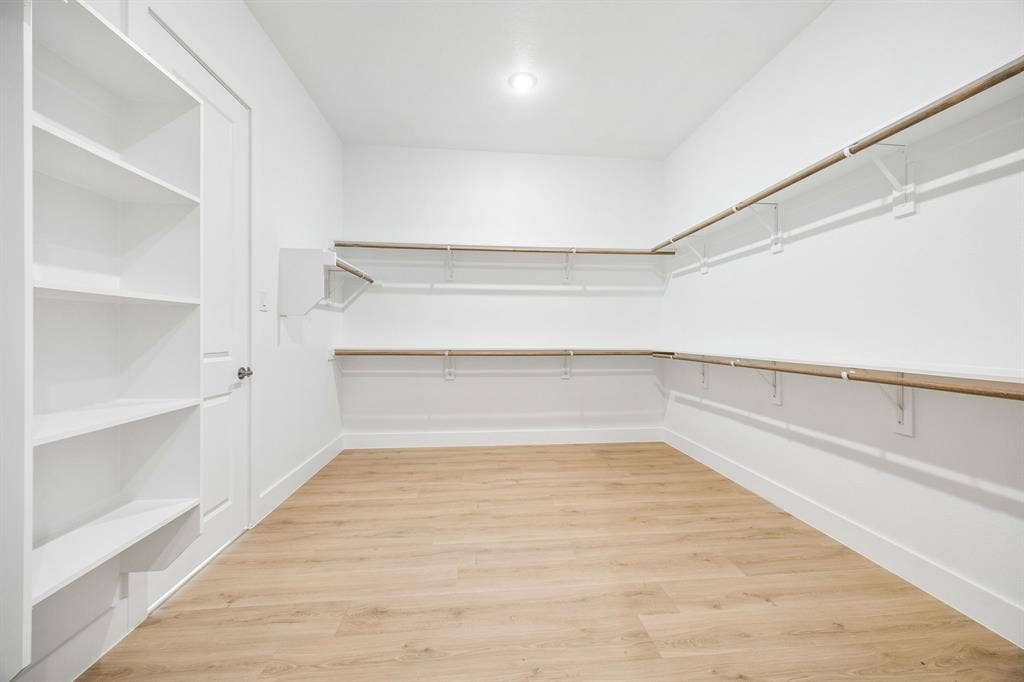 108 Swan Lake Drive, Waxahachie, TX 75165 Walk-in closet featuring wood-finish flooring, built-in shelving unit, dual-level wall-mounted shelving with integrated hanging rods, and recessed lighting