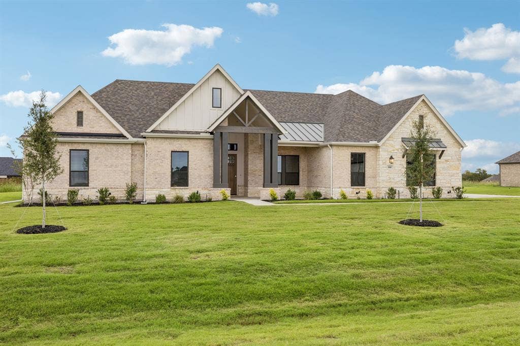 108 Swan Lake Drive, Waxahachie, TX 75165 Light-colored brick exterior featuring board-and-batten siding accents, metal roof detailing, a prominent gabled entryway, and dark-framed windows