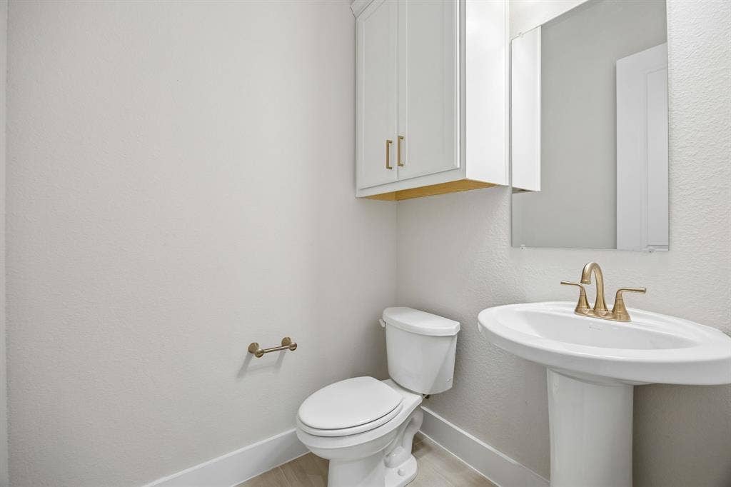 108 Swan Lake Drive, Waxahachie, TX 75165 White pedestal sink with a metallic widespread faucet, wall-mounted cabinet with gold-tone hardware, rectangular mirror, and toilet