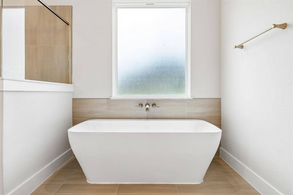 108 Swan Lake Drive, Waxahachie, TX 75165 Freestanding soaking tub featuring a wall-mounted brushed-finish faucet, neutral-toned tile surround, tile flooring, and frosted window