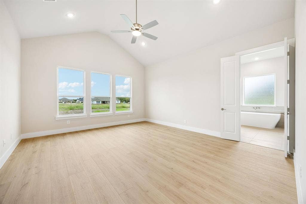 108 Swan Lake Drive, Waxahachie, TX 75165 Vaulted ceiling featuring a central brushed-nickel finish ceiling fan, wood-finish flooring, three oversized windows, and double doors opening to a space with a freestanding soaking tub