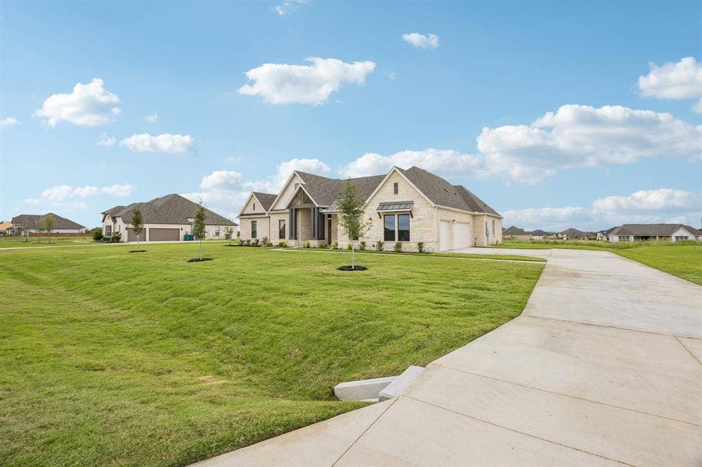 108 Swan Lake Drive, Waxahachie, TX 75165 Stone exterior residence featuring a multi-gabled roofline, metal roof accents, an extended concrete driveway, and a spacious front lawn