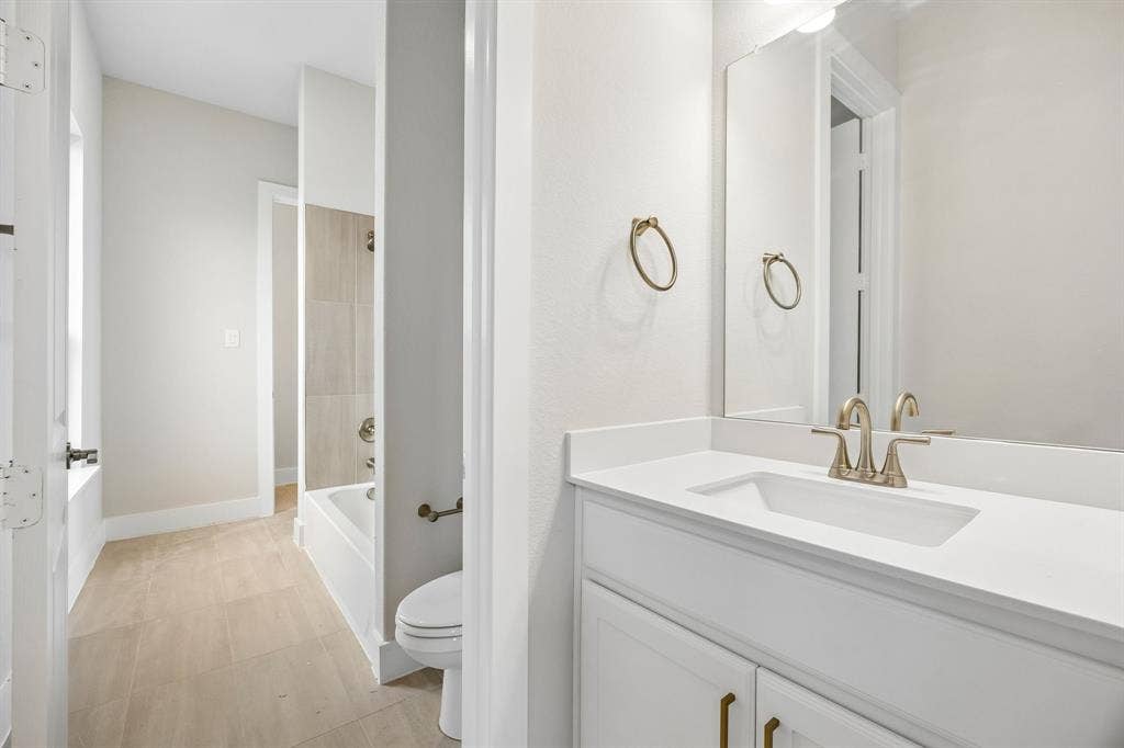 108 Swan Lake Drive, Waxahachie, TX 75165 White vanity with solid surface countertop and integrated rectangular sink, brushed metal faucet, full-height wall mirror, and neutral-tone tile flooring extending into the bathing area with tiled tub surround