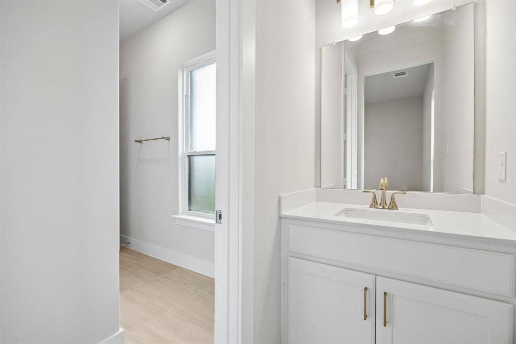 108 Swan Lake Drive, Waxahachie, TX 75165 Bathroom featuring a white vanity with a rectangular undermount sink, solid surface countertop, brass-finish faucet, and a wall-mounted mirror with multi-light fixture