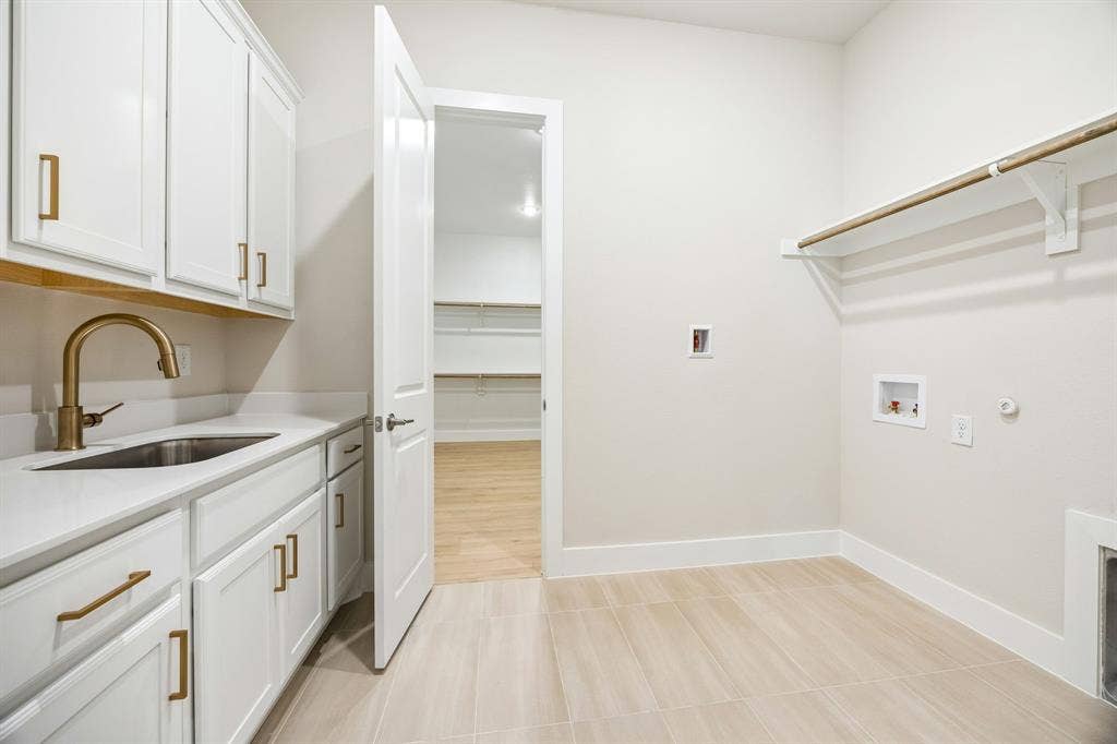108 Swan Lake Drive, Waxahachie, TX 75165 Laundry room featuring white cabinetry, a sink with brass-finish hardware, quartz countertops, tile flooring, and integrated wall shelving