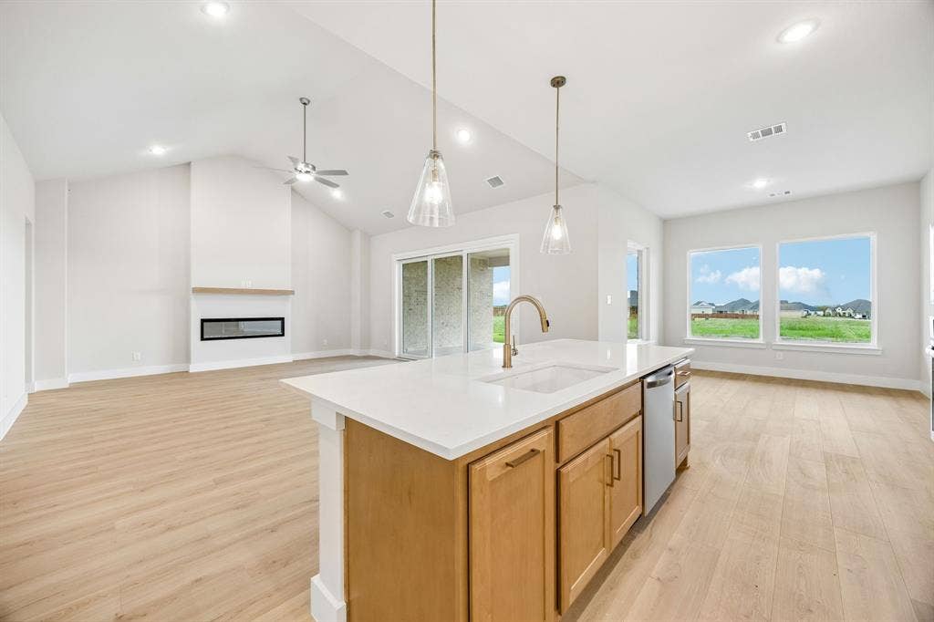 108 Swan Lake Drive, Waxahachie, TX 75165 Open-concept interior featuring vaulted ceilings, wood-finish flooring, a kitchen island with stone countertops, a linear fireplace, and recessed lighting