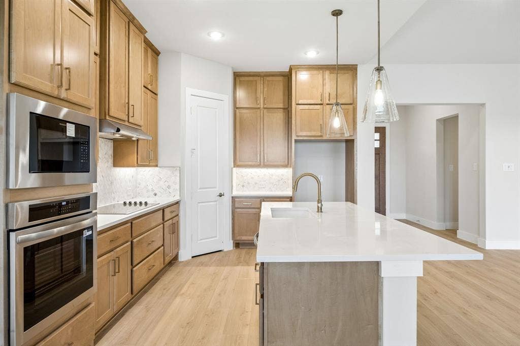 108 Swan Lake Drive, Waxahachie, TX 75165 Kitchen featuring wood-finish cabinetry, quartz countertops, a central island with an undermount sink, built-in stainless steel double ovens, and glass pendant lighting