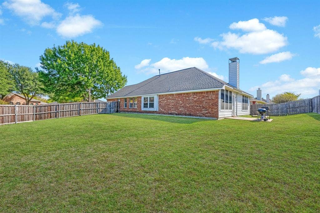 Expansive backyard featuring a brick exterior, shingled roof, exterior chimney, and perimeter wood fencing