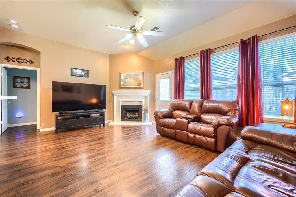 Living area featuring wood-finish flooring, vaulted ceilings, a fireplace with a white mantel, and a multi-blade ceiling fan