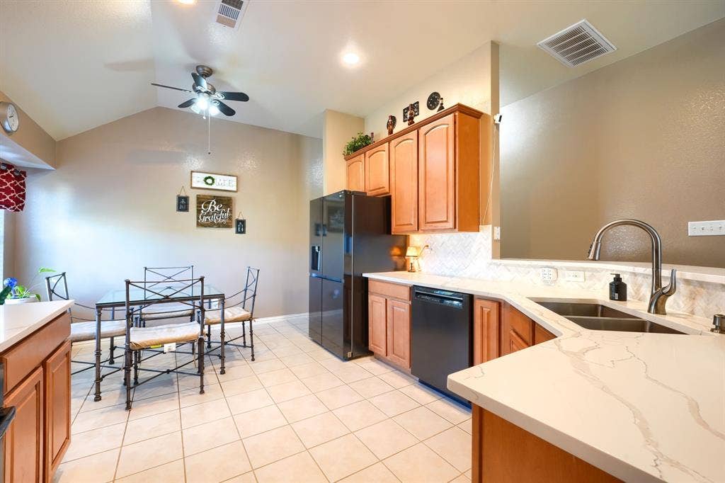 Kitchen featuring wood cabinetry, stone-finish countertops, tile flooring, a dual-basin stainless steel sink with a high-arch faucet, and black built-in appliances