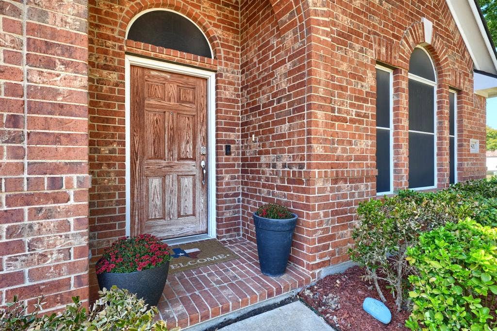 Red brick exterior featuring an arched entryway, a paneled wood-finish door with an arched transom window, and tall arched windows