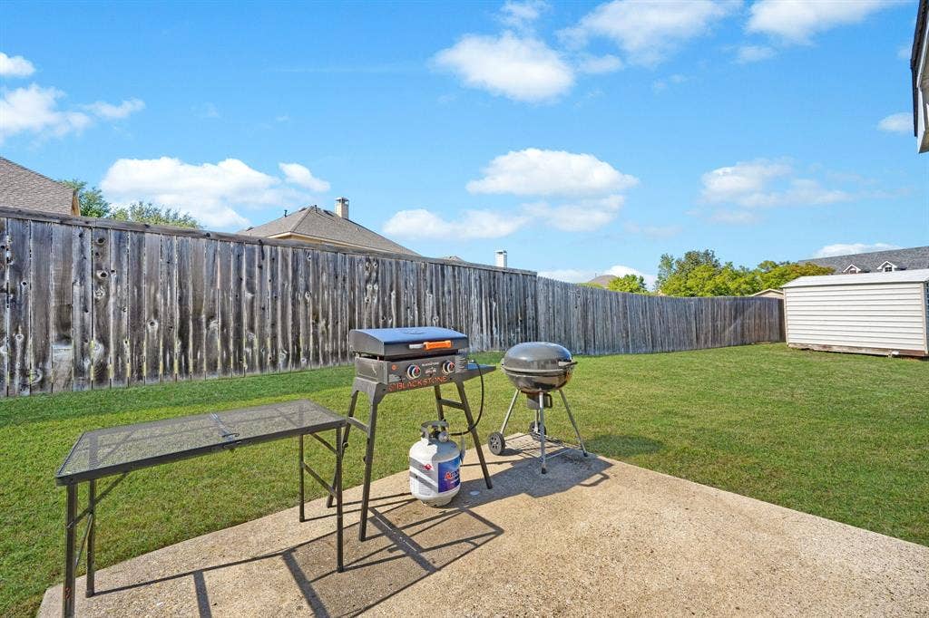 Backyard featuring a concrete patio, wood privacy fencing, a maintained lawn, and a detached storage shed