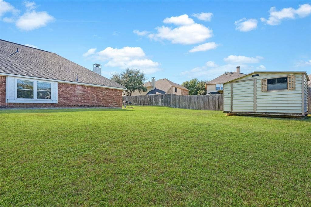 Expansive backyard featuring a brick exterior facade, large lawn, wood fencing, and a detached storage structure