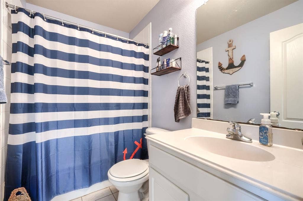 Bathroom featuring a white vanity with a integrated countertop and basin, chrome faucet hardware, wall-mounted mirror, and tile flooring