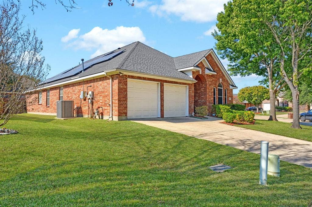 Single-story brick exterior featuring a roof-mounted solar panel array, a two-car garage, and an arched entryway