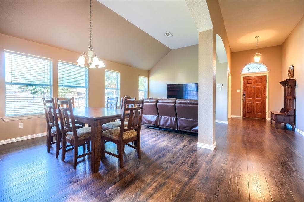 Vaulted ceilings, wood-finish flooring, multi-pane windows with horizontal blinds, decorative pendant lighting, and an arched entryway with a solid wood door featuring a fanlight transom