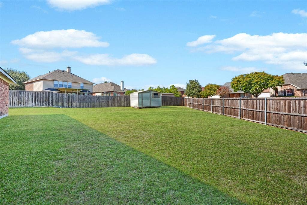 Expansive backyard featuring a level lawn, full wood-plank privacy fencing, and a detached storage shed