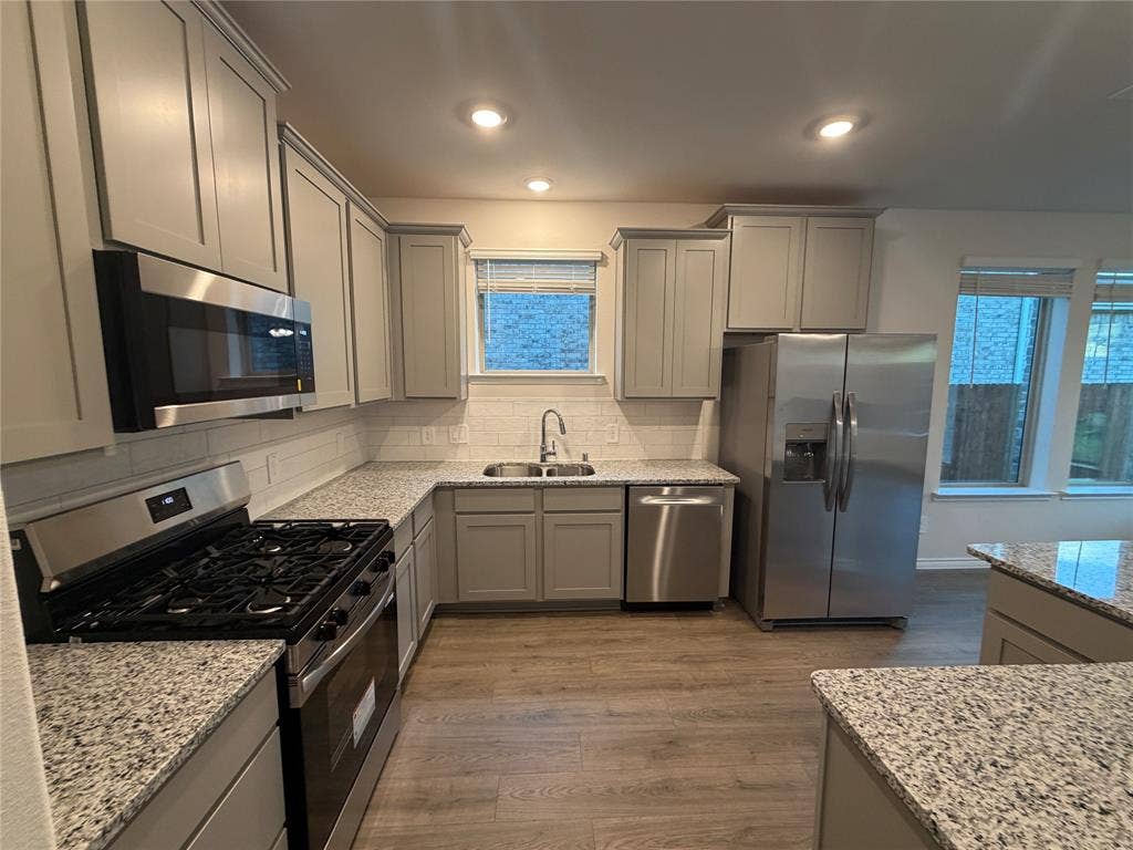 Kitchen featuring light-gray shaker-style cabinetry, speckled stone-finish countertops, stainless steel appliances, recessed ceiling lighting, and wood-finish flooring