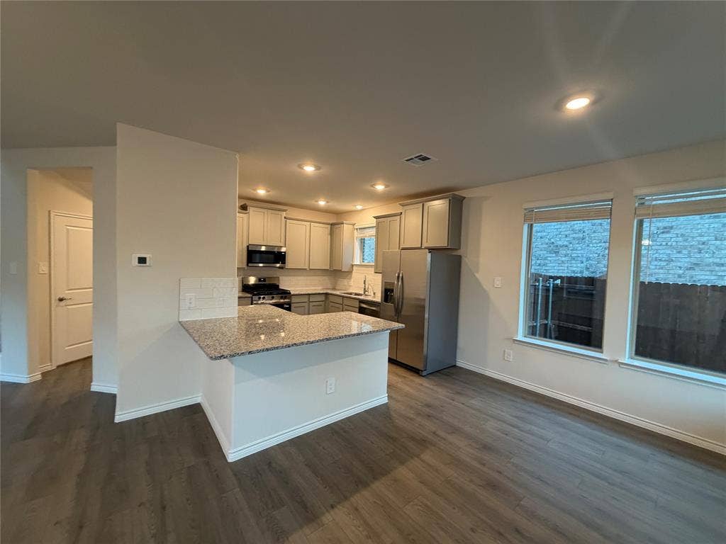 Kitchen featuring wood-finish flooring, stone-surfaced countertops, a breakfast bar, recessed lighting, and stainless steel appliances