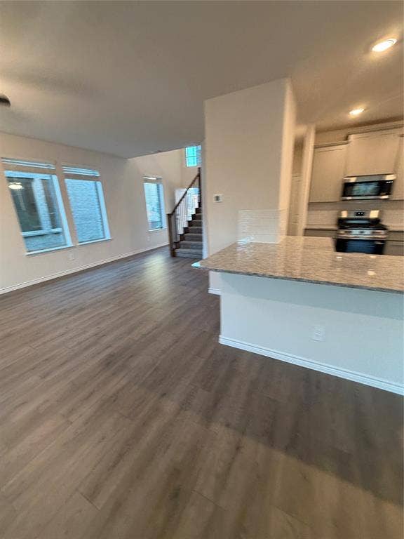 Open-concept kitchen featuring a stone-topped island, wood-finish flooring, recessed lighting, and large windows