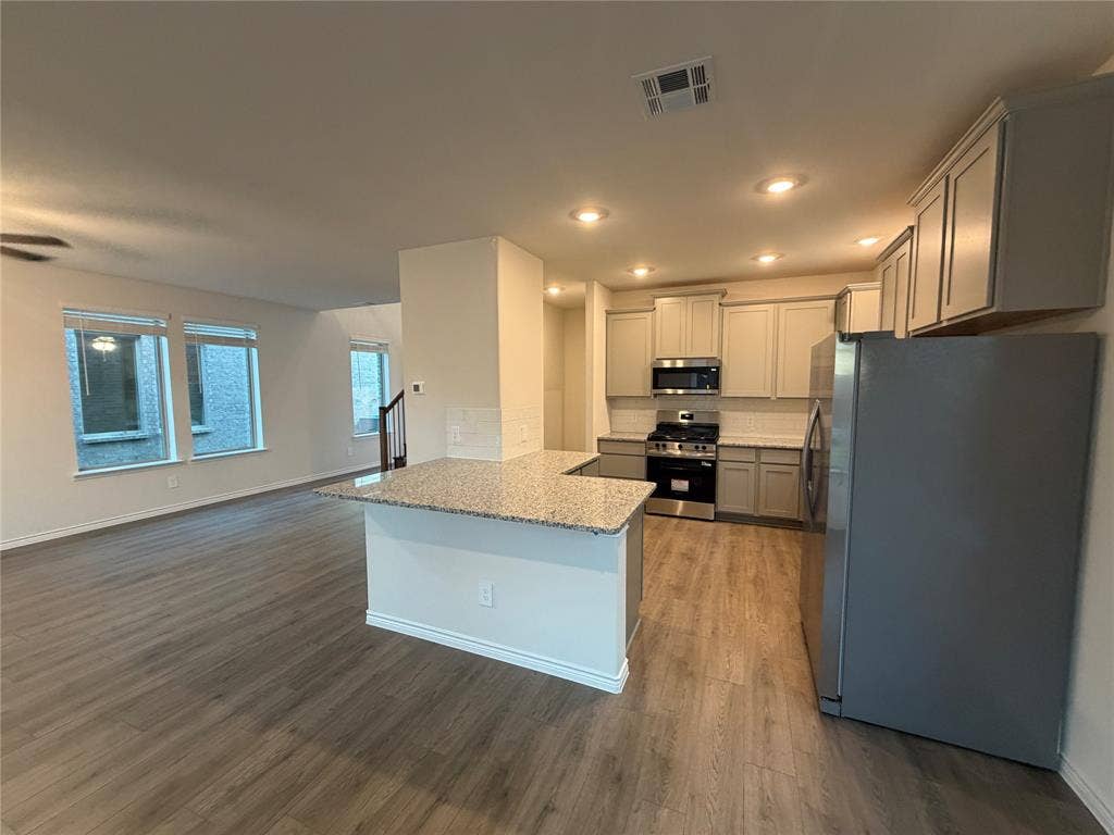 Kitchen featuring a peninsula with stone-finish countertops, stainless steel appliances, recessed lighting, and wood-finish flooring