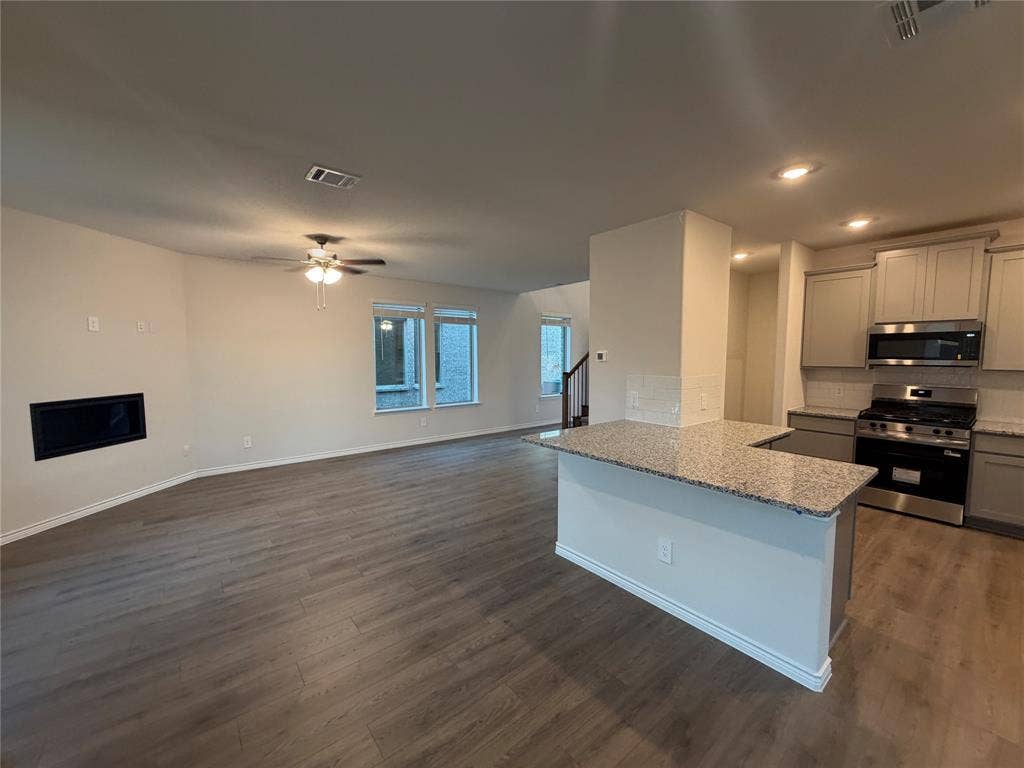 Open concept living area featuring wood-finish flooring, a kitchen island with stone countertops, stainless steel appliances, and a built-in fireplace