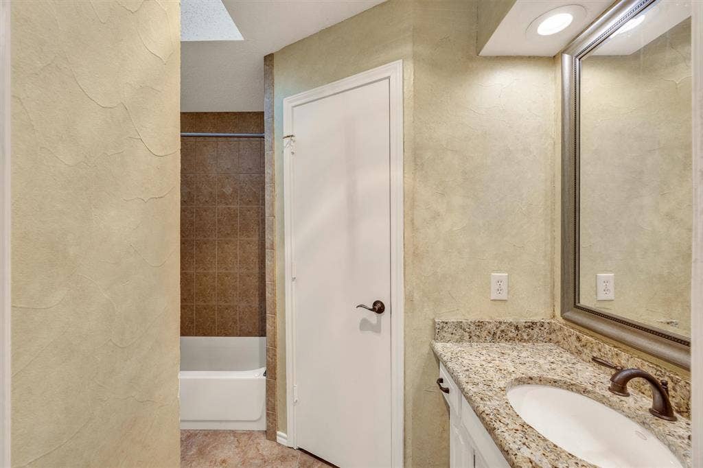 1025 Brownfield Drive, Mesquite, TX 75150 Bathroom featuring a stone-patterned vanity countertop, integrated sink with oil-rubbed bronze fixtures, textured wall finish, and a tub with tiled surround