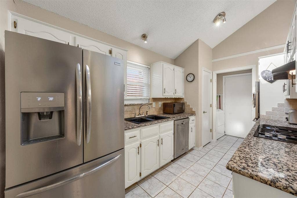 1025 Brownfield Drive, Mesquite, TX 75150 Kitchen featuring vaulted ceilings, stainless steel refrigerator and dishwasher, stone-finish countertops, tile flooring, and white cabinetry