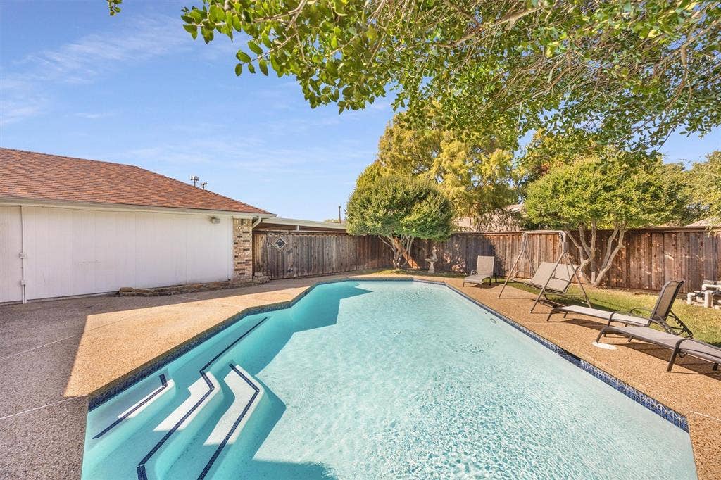 1025 Brownfield Drive, Mesquite, TX 75150 In-ground swimming pool with a stepped entry, surrounded by a textured aggregate pool deck, enclosed by a wood privacy fence