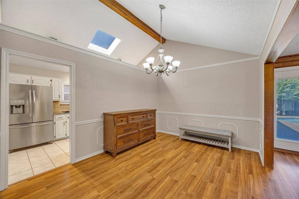 1025 Brownfield Drive, Mesquite, TX 75150 Vaulted ceiling with exposed wood beam, skylight, decorative chair rail molding, and multi-arm chandelier