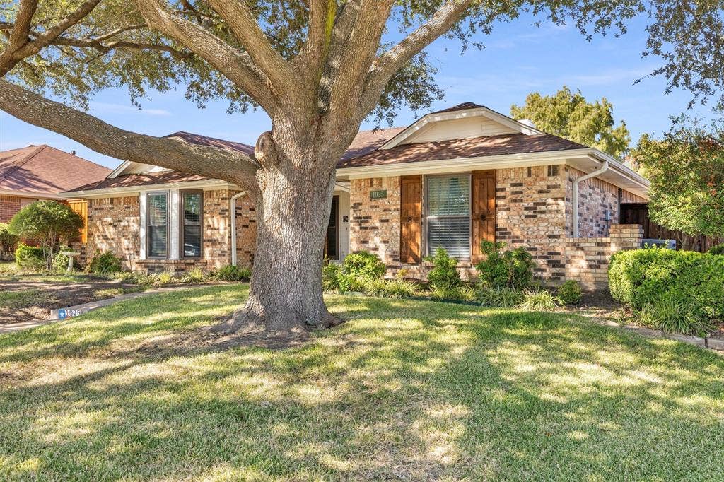 1025 Brownfield Drive, Mesquite, TX 75150 Single-story brick exterior featuring wooden shutters, a multi-gabled roofline, and a mature shade tree on a grass lawn