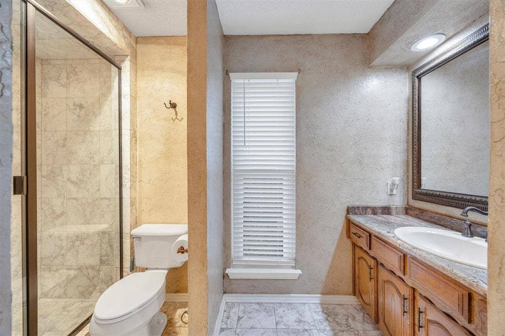 1025 Brownfield Drive, Mesquite, TX 75150 Bathroom featuring a walk-in shower with tiled surround, a vanity with stone-finish countertop, a drop-in sink, and framed wall mirror