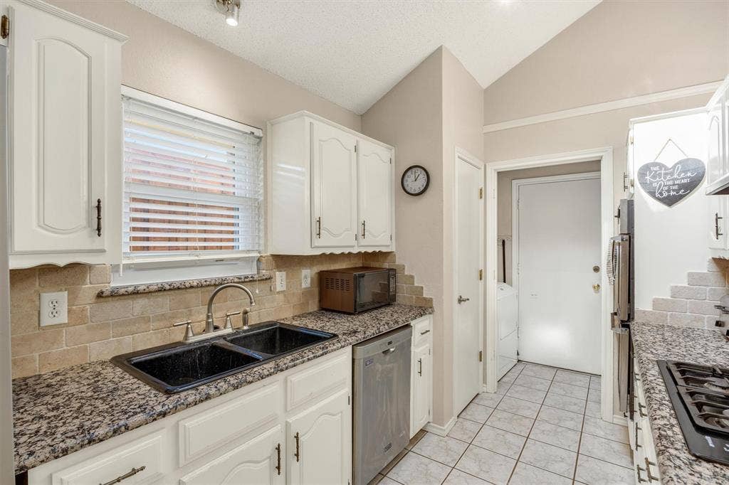 1025 Brownfield Drive, Mesquite, TX 75150 Kitchen featuring white cabinetry, stone-finish countertops, tiled backsplash, double-basin drop-in sink, and stainless steel built-in dishwasher