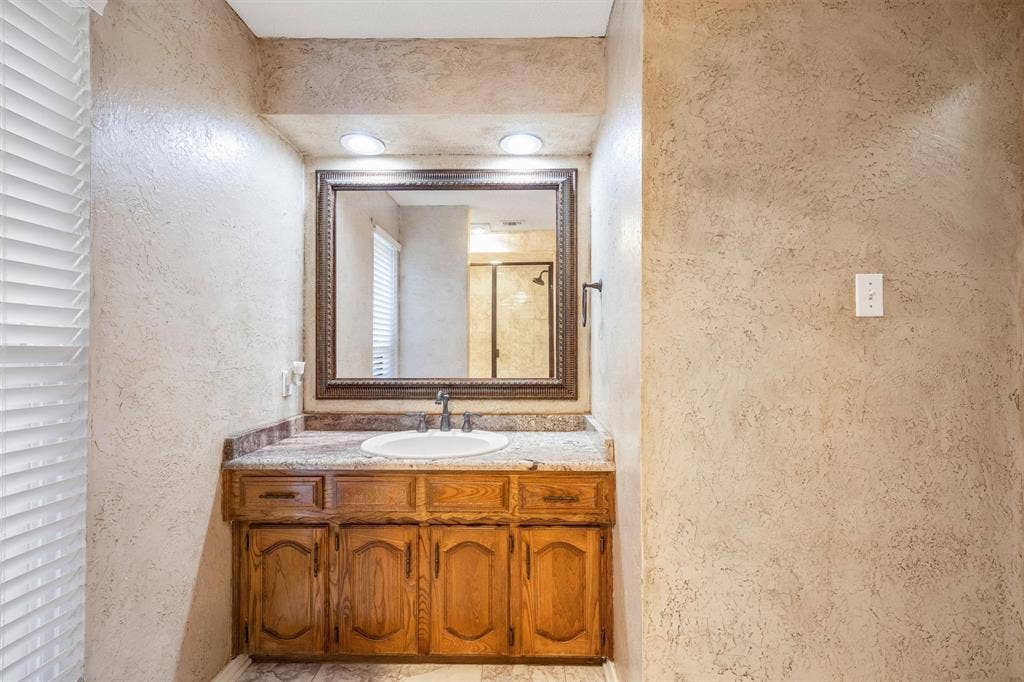 1025 Brownfield Drive, Mesquite, TX 75150 Wood vanity with a natural stone countertop, undermount oval sink, dark metal faucet, and large framed mirror with recessed lighting