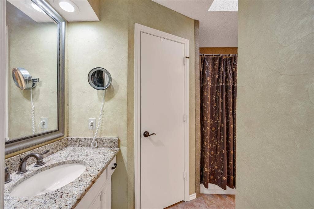 1025 Brownfield Drive, Mesquite, TX 75150 Vanity featuring a stone-composite countertop, undermount oval sink, and metallic faucet hardware, paired with a framed wall-mounted mirror, recessed lighting, and a textured wall finish