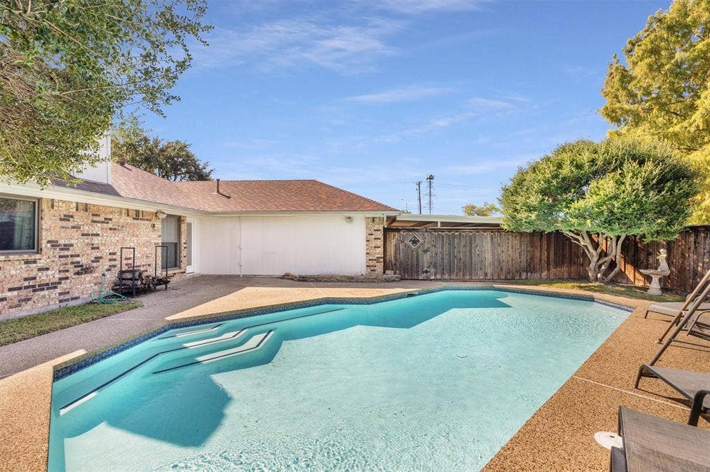 1025 Brownfield Drive, Mesquite, TX 75150 In-ground swimming pool with built-in steps, expansive aggregate concrete patio, brick exterior facade, and wood privacy fencing