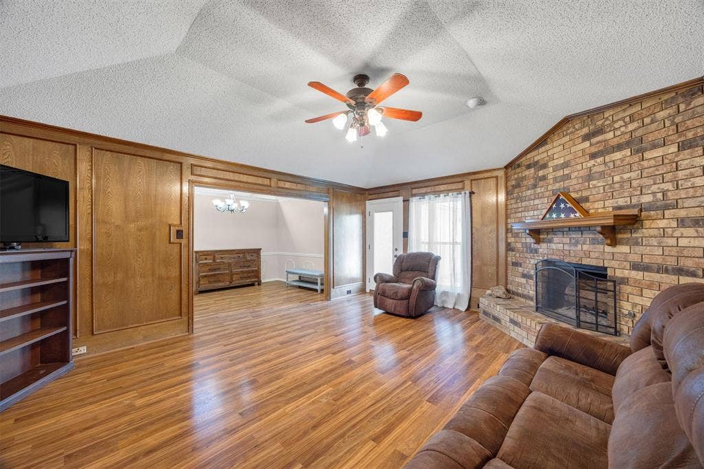 1025 Brownfield Drive, Mesquite, TX 75150 Vaulted ceiling, floor-to-ceiling wood paneling, wood-finish flooring, and a brick fireplace featuring a wood mantel